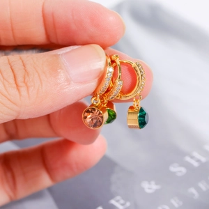 Primer plano de pendientes chapados en oro con colgantes de circonita de colores en mano