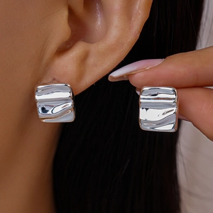 Macro shot of silver square stud earrings with irregular wavy texture on a model's ear