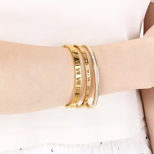 Close-up of stacked gold titanium steel bracelets with Roman numerals and pavé crystal details