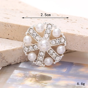 Detail of 2.5cm silver brooch with white pearls and rhinestones on stone background