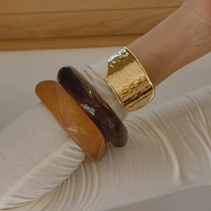 Dettaglio del bracciale a onde dorate e bracciali in resina sopra una manica in maglia