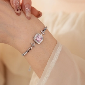 Detail of a silver chain bracelet featuring a pink square zircon and cross links on wrist