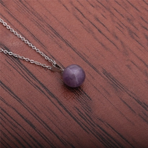 Close-up of a minimalist round purple stone pendant on a silver chain over wood