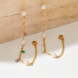 Elegant gold chain bracelet with white pearls and colorful gemstones on a stone surface