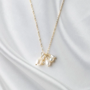 Detail view of five baroque freshwater pearls on a delicate gold chain over white silk