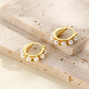 Elegant U-shaped golden hoop earrings featuring multiple white pearls on a beige stone slab