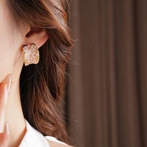 Gros plan de boucles d'oreilles dorées en forme de C avec relief floral rose sur un mannequin