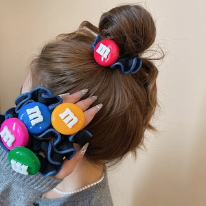 Détail d'un pendentif en résine colorée avec lettre m sur un chouchou en tissu noir plissé