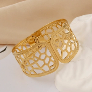Macro detail of a wide gold-plated bangle with geometric honeycomb cutout design