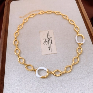 Detail of gold oval link necklace with white enamel accents on rustic linen background