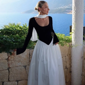 Detail of off-shoulder black knit top and white satin patchwork dress on a sunlit balcony