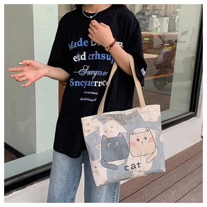 Detail view of large beige canvas tote bag with cartoon cat print and shoulder strap