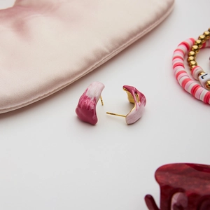 Detail of irregular pink marble resin earrings with gold metal posts on silk fabric