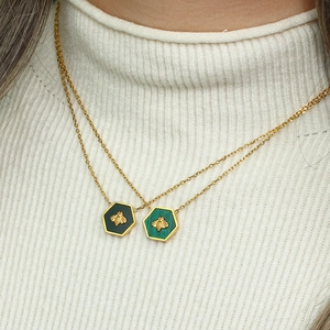 Gold hexagon bee pendant necklace set in black and green colors worn on white sweater