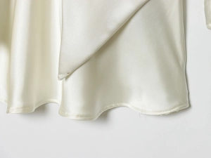 Detail of champagne satin dress showing wave-like draped hem and premium silk texture