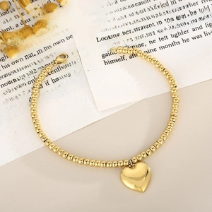 Detail of a gold stainless steel beaded bracelet with a polished heart charm