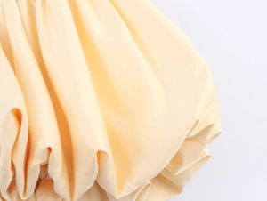 Gros plan sur le tissu satiné crème montrant les plis de l'ourlet et la texture