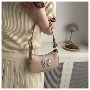 Close-up of beige handbag featuring a silver metallic bow and knotted strap detail