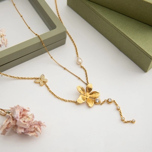 Detailansicht der 18K Gold Schmetterling-Blumen-Halskette mit Perlen auf einer Geschenkbox