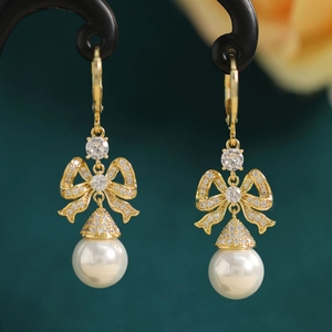 Macro view of gold bow-knot pearl earrings with sparkling zircon inlay details