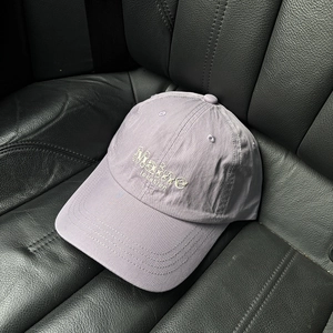 Détail de casquette en coton lilas avec broderie Maine posée sur un siège de voiture