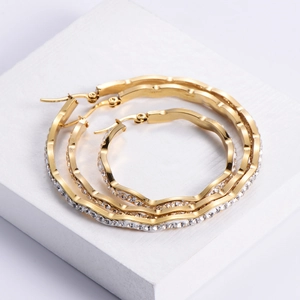 Three pairs of wavy gold hoop earrings with inset crystals on white textured stone