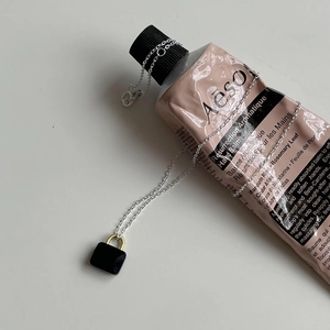 Detail of a minimalist padlock necklace with black polished pendant and gold accents