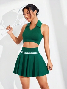 Dettaglio del top allacciato al collo verde scuro e gonna a pieghe con logo GYMWEAR