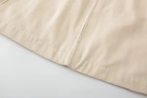 Close-up of beige twill jacket hem showing high-quality stitching and metal zipper