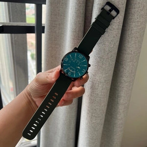 Close-up of hand holding a green dial quartz watch with black case and silicone strap