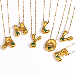 Detail of 18k gold plated bubble letter necklaces with green heart gemstones