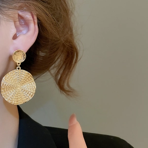 Close-up of golden geometric round drop earrings featuring textured hammered metal finish