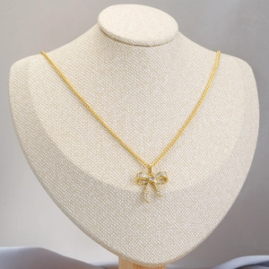 Goldene Schleife-Halskette mit weißen Zirkonia auf Modell vor beigem Hintergrund