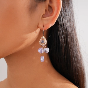 Close-up of model wearing gold drop earrings with purple crystals and hollow heart design
