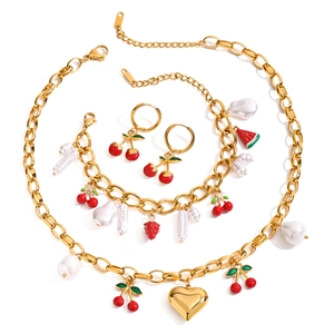 Détails de l'ensemble de bijoux en perles dorées avec pendentifs cerise et cœur sur fond blanc