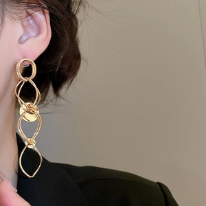 Detailed close-up of golden geometric linked tassel earrings worn by a model