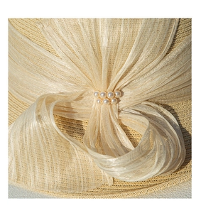 Détail du chapeau en paille tressée beige avec nœud en maille et décorations en perles