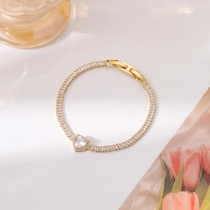 Detail of gold bracelet featuring rectangle and heart-shaped zircons on aesthetic background