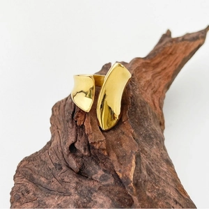 Polished 18K gold-plated titanium steel wavy open ring on a dark wooden branch background