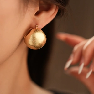 Detail of chunky gold hoop earring with textured matte finish on a model's ear