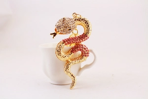 Close-up of a crystal snake keychain with gold finish and pink rhinestones on a cup