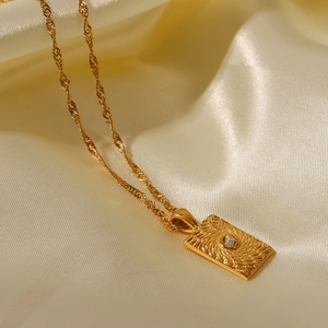 Détail d'un pendentif rectangulaire doré avec texture rayonnante et pierre de zircon