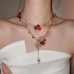 Detail of layered gold necklace with red petals and translucent organza leaf charms