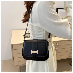 Detail view of a black leather crossbody bag with a golden H buckle worn by a model