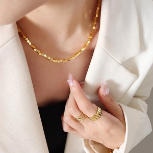 Minimalist gold jewelry set including bead chain necklace and textured rings on a model