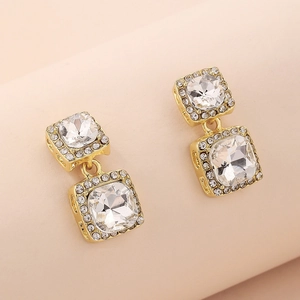 Detail of square gold earrings featuring centered rhinestones and hollow side patterns