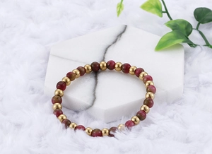 Detail of garnet beads and gold titanium steel bracelet on white marble display tray