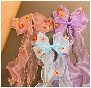 Detailed view of three organza bow hair clips in pink, purple, and blue with felt flowers