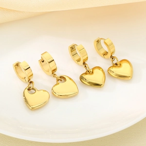 Detailed view of polished gold heart dangle earrings on a white plate with satin fabric
