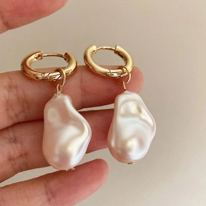 Macro shot of gold hoop earrings with Baroque pearl drops held against a soft background